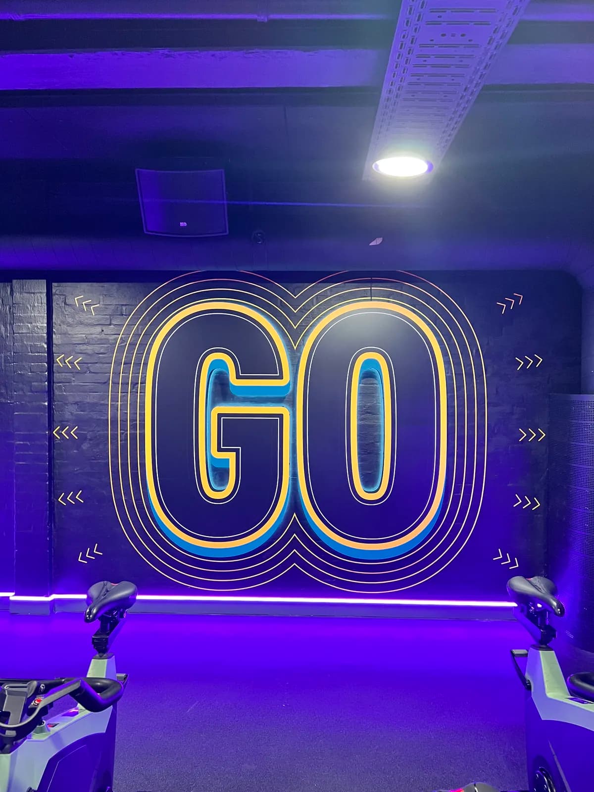 Stor vægdekoration med 'GO' i retro-neonlook i cykelsal med lilla LED-belysning