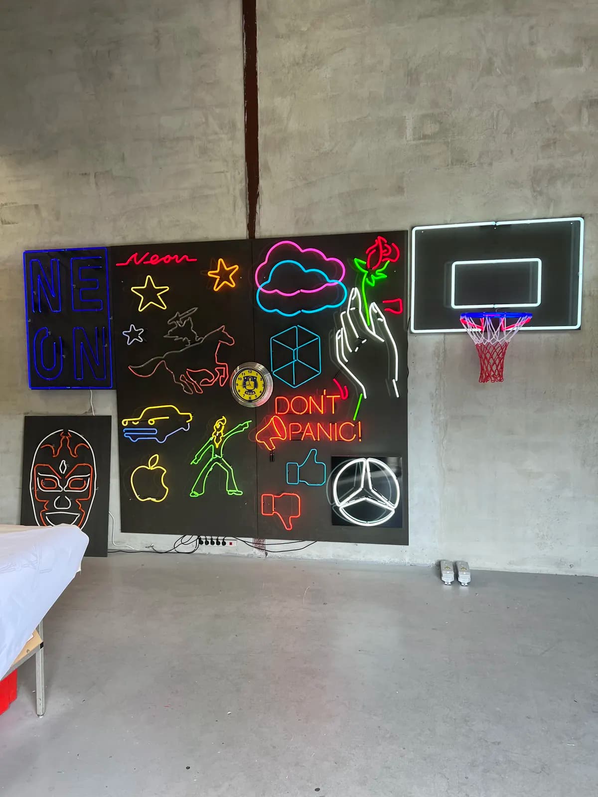Udstillingsvæg med LED-neonfigurer i værkstedet, heriblandt Mercedes-stjerne, basketkurv og 'Don't panic'