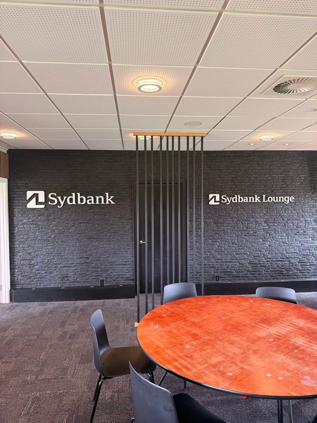Hvide bogstaver til Sydbank Lounge monteret på sort stenvæg i loungeområdet