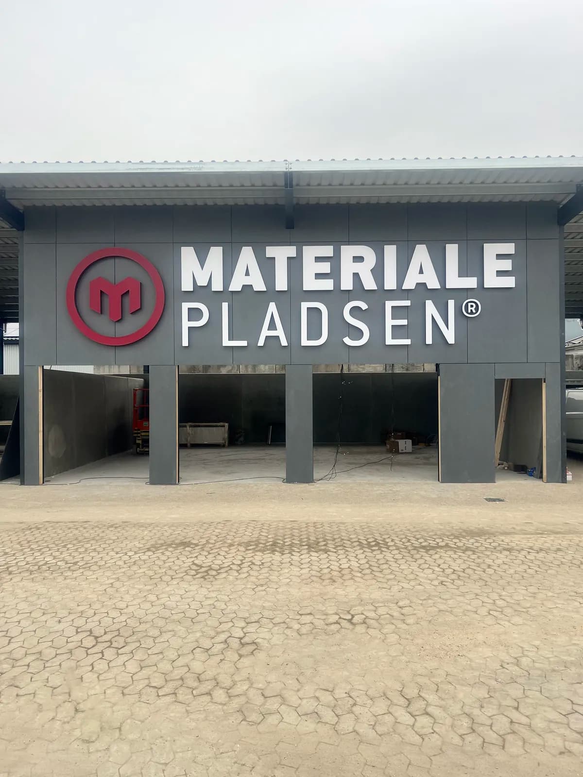 Facadebogstaver og logo i rødt til MaterialePladsen monteret på grå facade