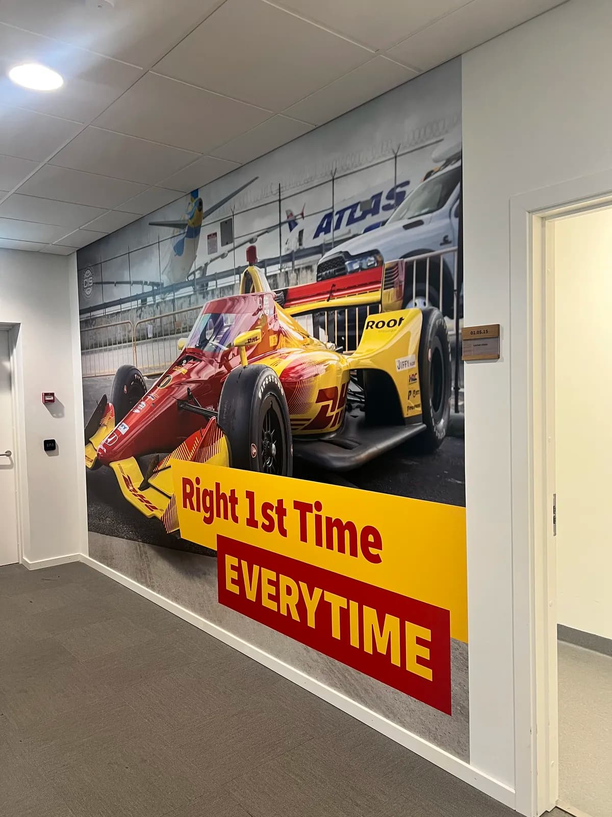 Printet vægfolie i fuld højde med DHL-racerbil og sloganet Right 1st Time Everytime hos DHL Express