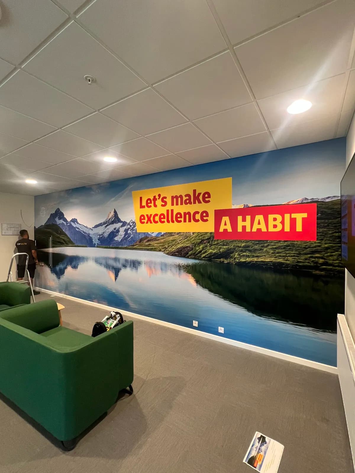 Panoramisk vægfolie med bjerglandskab og motivationsslogan i pauseområdet hos DHL Express