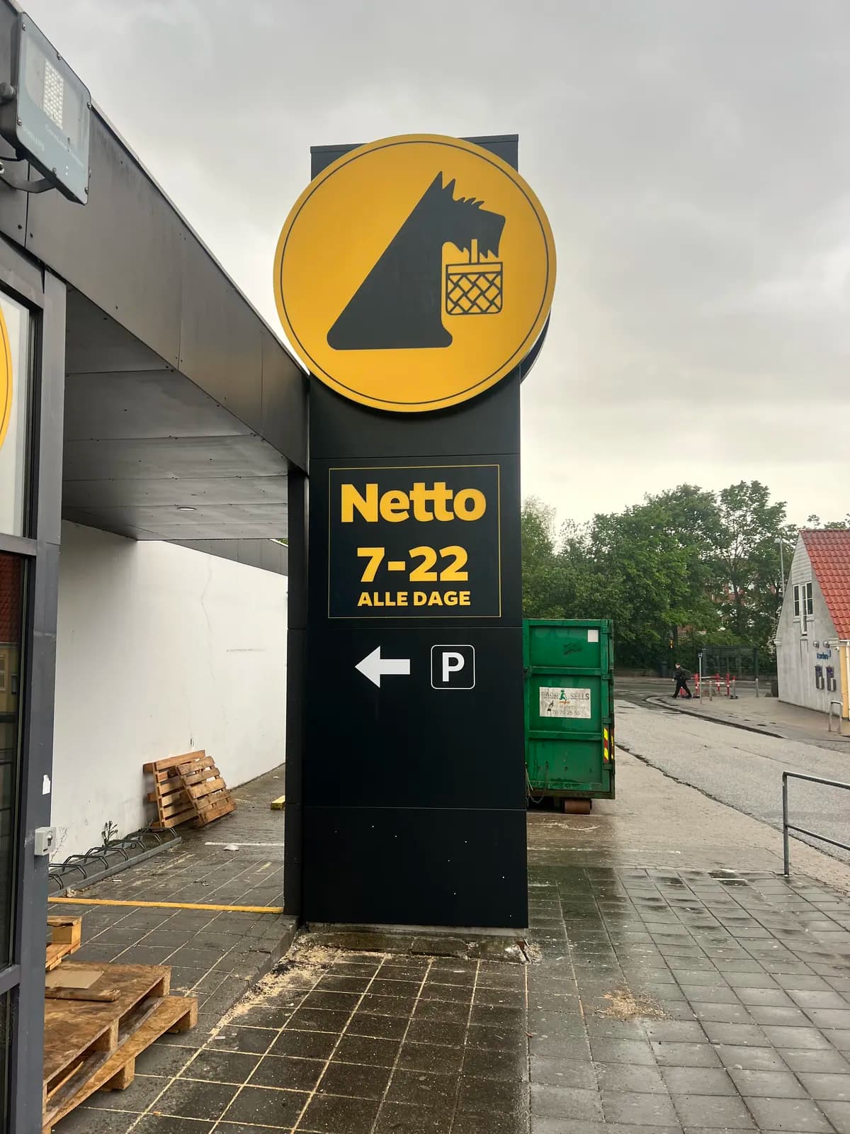 Pylonskilt med rundt logoskilt, åbningstider og parkeringshenvisning til Netto set forfra