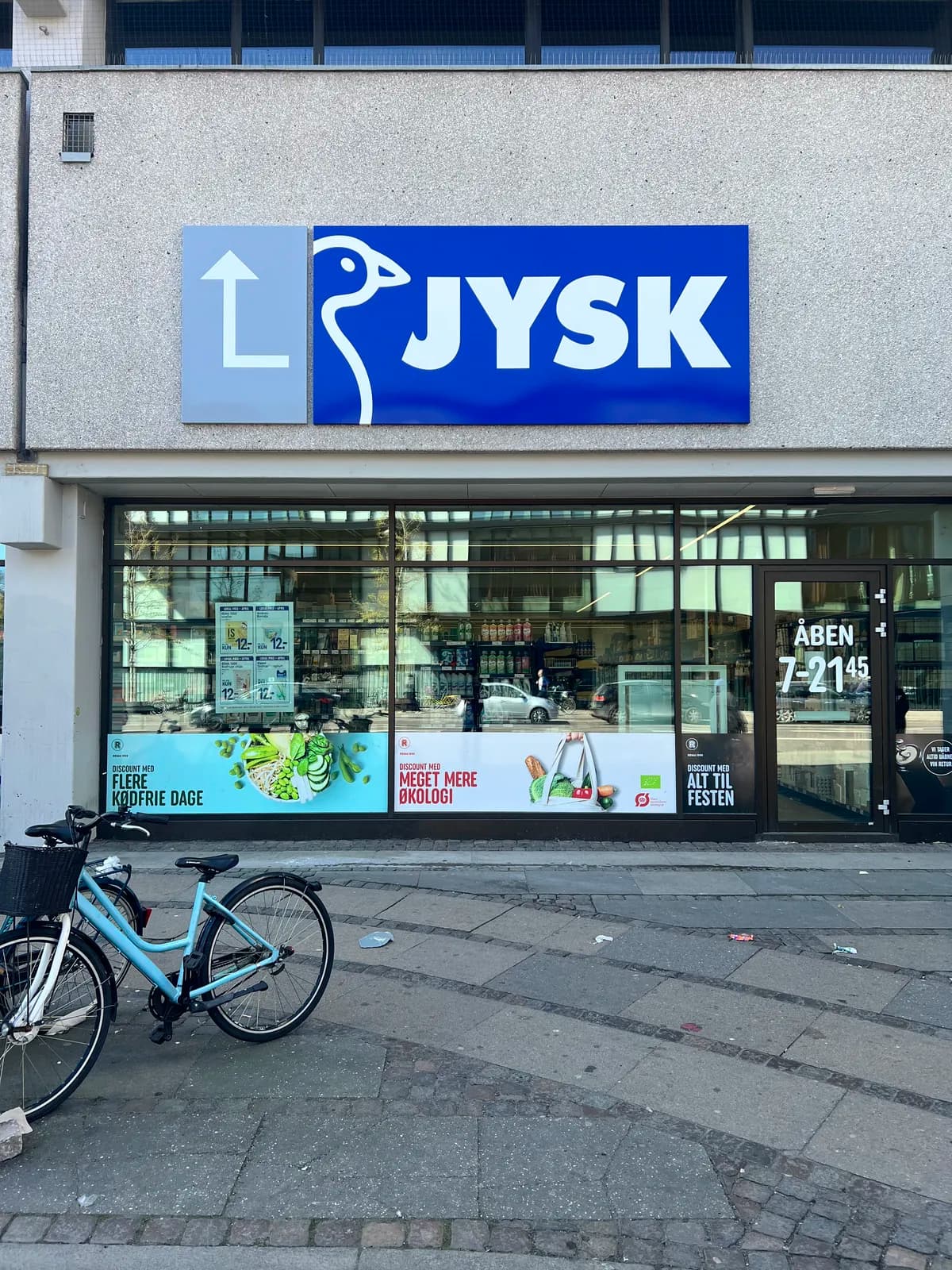 Facadeskilt med JYSK-logo og henvisningspil monteret på granitfacade i gadeplan