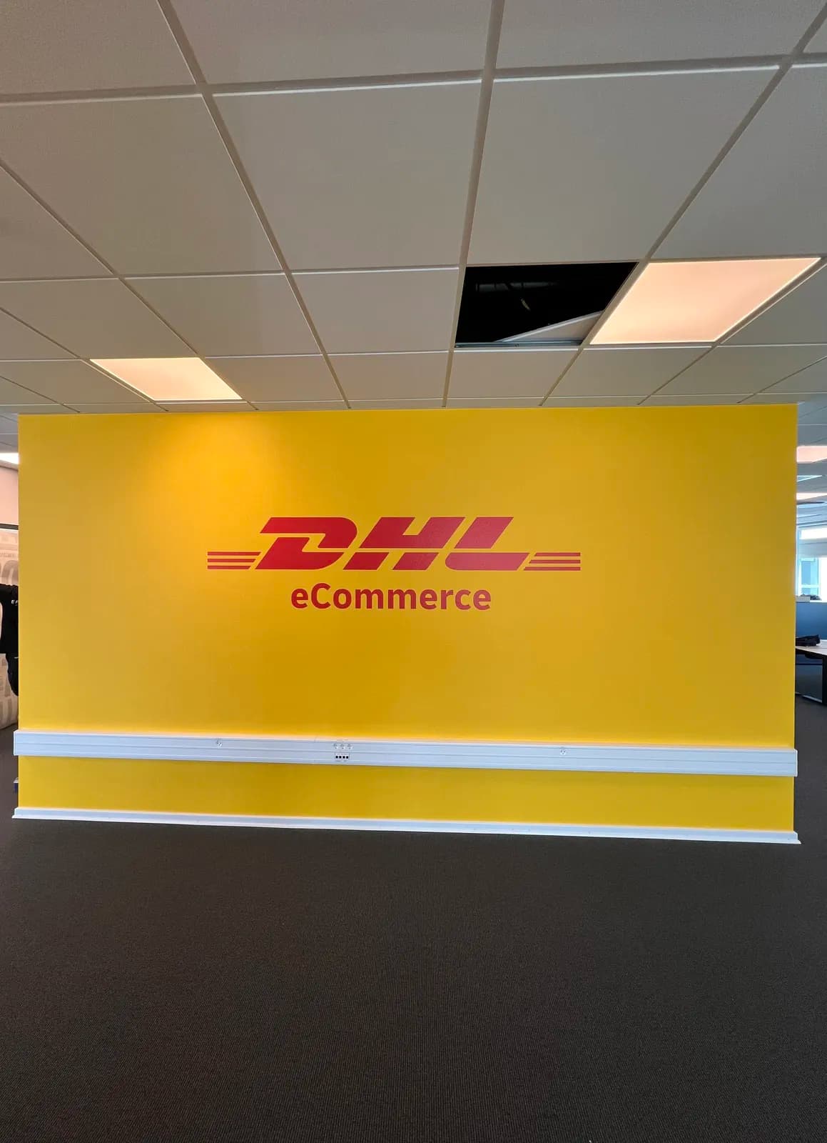 Vægfolie med DHL eCommerce-logo monteret på gul væg i kontorindretning