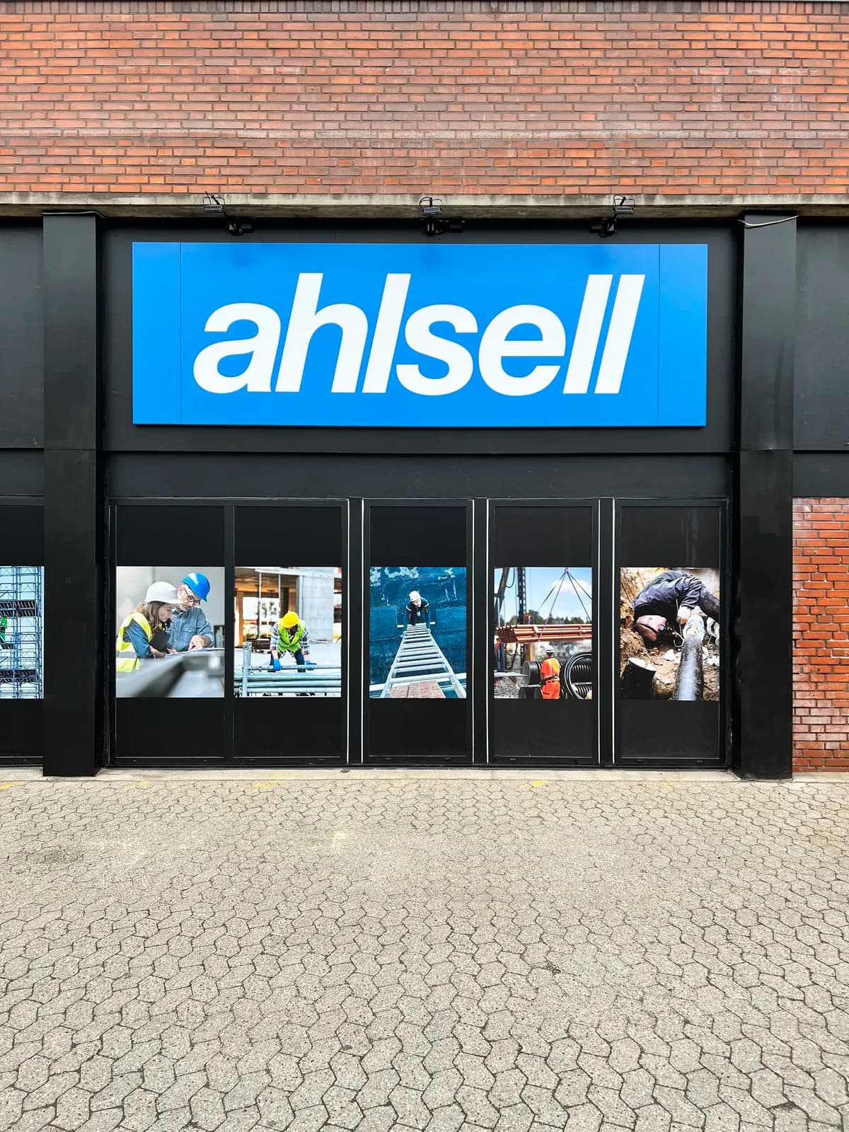 Facadeskilt til Ahlsell med projektørbelysning på sort facade og printede vinduespartier